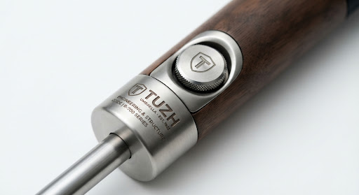 Detail shot of customized metal hardware on an umbrella, showing engraved logos on the ferrule and button. High-end industrial photography, sharp focus, metallic textures against a crisp white background.